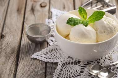 Rustik ahşap arka plan üzerinde beyaz kase vanilyalı dondurma ile nane yaprakları