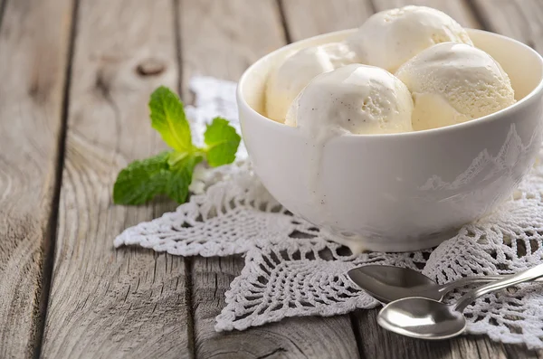 Rustik ahşap arka plan üzerinde beyaz kase vanilyalı dondurma ile nane yaprakları