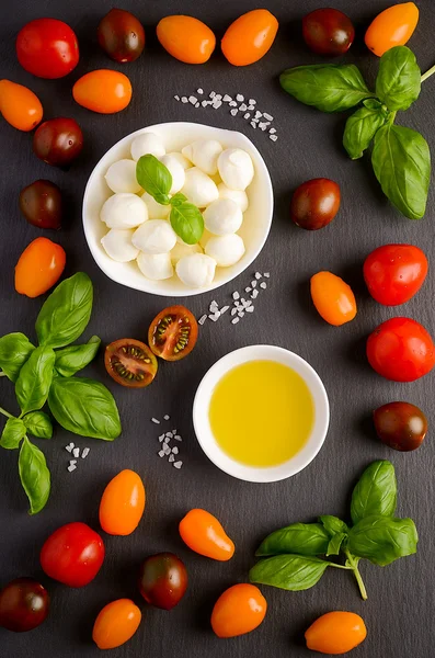 Italian food ingredients  mozzarella, tomatoes, basil and olive oil on black background — Stock Photo, Image