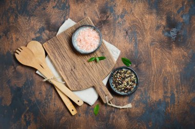 Ahşap mutfak aletleri ve baharatlar. Tahta kaşıklar, tahta kesme tahtası, eski bir masa üzerindeki peçete ve baharatlar. Üst görünüm, alanı kopyala.