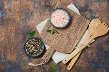 Ahşap mutfak aletleri ve baharatlar. Tahta kaşıklar, tahta kesme tahtası, eski bir masa üzerindeki peçete ve baharatlar. Üst görünüm, alanı kopyala.