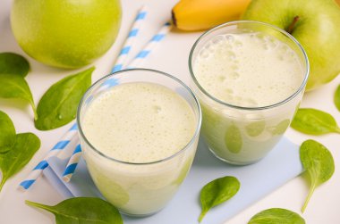 Elma, muz ve ıspanak üzerinde beyaz bir arka plan ile yeşil smoothie.