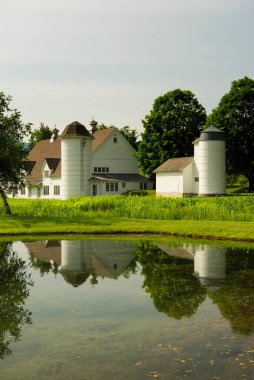 Vermont 'ta bulutlu bir günde gölde yansıyan beyaz çiftlik binaları.