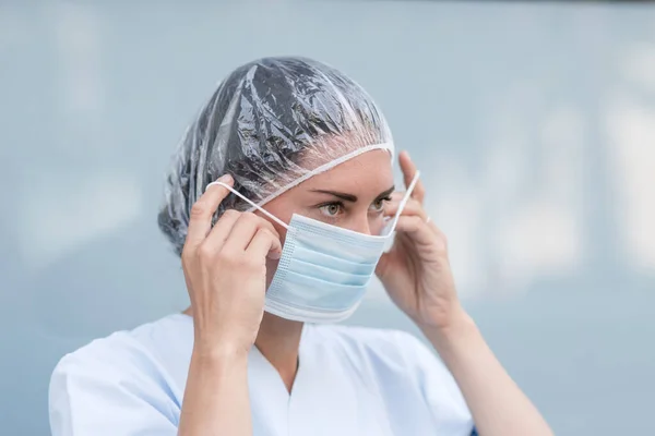 Portrait of a woman doctor putting on and fixing her surgical protective mask before her work shift