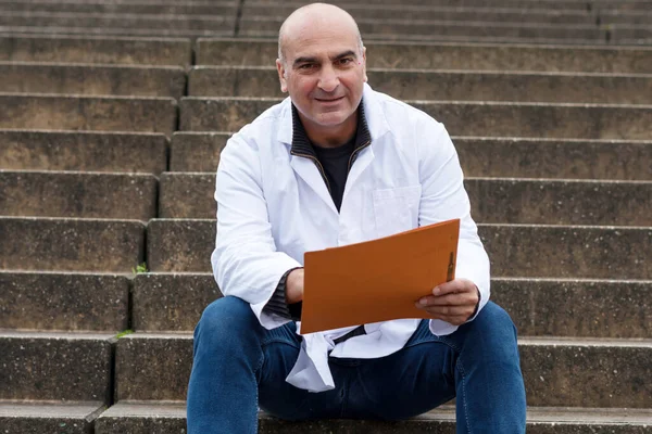 Smiling medical doctor or dentist sitting on outdoor stairs and holding a clinical study report