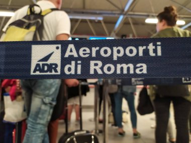 Fiumicino, İtalya - 30 Eylül 2019: ADR Aeroporti di Roma bayrağı. Arka planda, bavullarıyla odaklanmış gezginlerden. Seçici odak