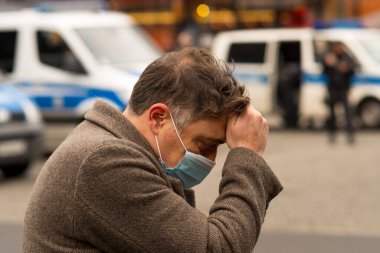 Kötü haber ya da baş ağrısı yüzünden elleri başının üstünde tıbbi koruyucu maske takan bir adam. Coronavirus COVID-19 SARS-CoV-2 enfeksiyonuna karşı koruma. Önplanda seçmeli odak