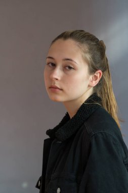 Gri bir arkaplandan kameraya bakan at kuyruklu güzel bir kızın yarı profil portresi.