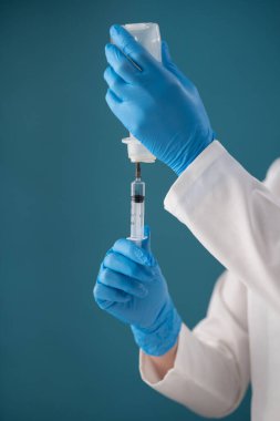 Mavi arka planda beyaz önlüklü bir hemşire tıbbi bir maddeyi şırıngaya sokuyor..