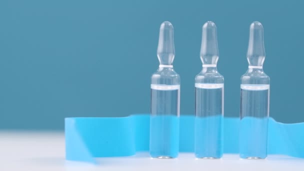 Ampoules en verre avec un médicament pour les virus sur un fond bleu sont sur la table. — Video
