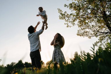 Mutlu genç ebeveynler yazın yeşil çimlerde kızlarıyla oynarlar..