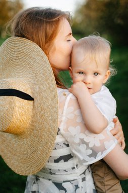 Sevgi dolu genç bir anne, bebeği kucağına alır ve ona sarılır. Çocuk kameraya bakar..