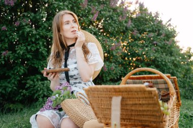 Pikniğe giden genç bir kız parkta yeşil çimlerin üzerinde otururken taze yaban mersini yiyor..