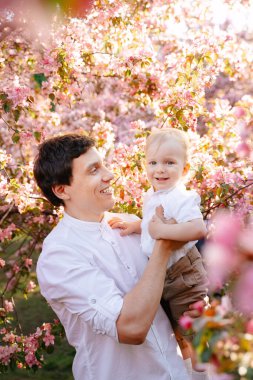 Mutlu bir baba ve oğulun portresi parkta çiçek açan bir bahçenin arka planına karşı..