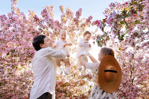 Parents with children play against the backdrop of greenery in the garden in summer.