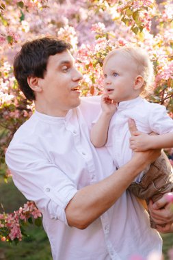 Baba kollarında bir çocukla, çiçek açan bir elma ağacının arka planında
