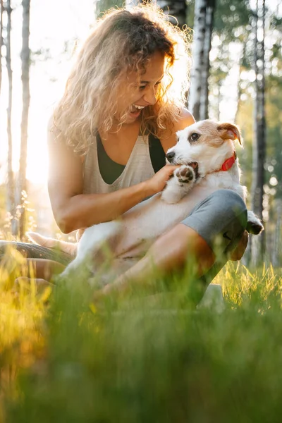Kıvırcık saçlı kadın parkta köpek Jack Russell 'la oynuyor..