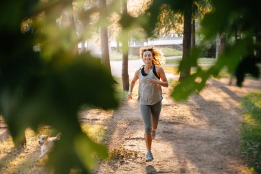 Gülümseyen genç bir kız orman yolunda koşuyor..