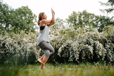 Spor kıyafetli çekici bir kadın yoga yapıyor, tek ayak üstünde egzersiz yapıyor.