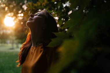 Yeşil ve güneş ışığının arka planında sarı kazaklı genç bir kadın..
