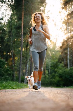 Genç, narin bir kız parkta bir köpekle spor yapıyor..