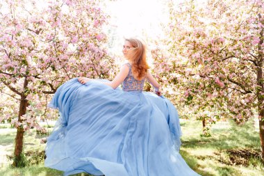 Kırmızı saçlı, mavi ipek elbiseli bir kadın bahçede koşuyor..