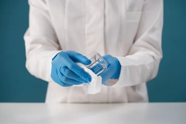 Verpleegster in kamerjas voert desinfectie uit door beschermende brillen af te vegen Stockafbeelding
