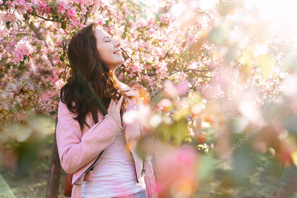 A young woman stands dreamily in an apple orchard in bloom.