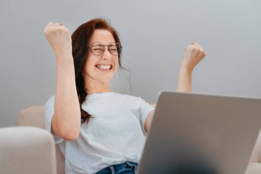 Genç bir kadın elinde bir dizüstü bilgisayarla zafere seviniyor..