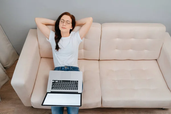 Young woman relaxes sitting on the sofa after doing work on a laptop
