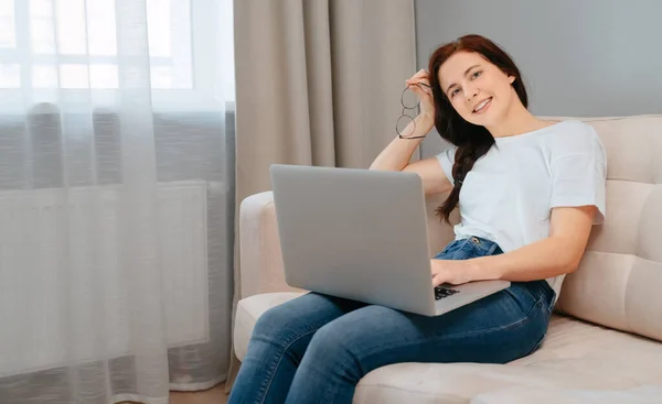 프리랜서 여성은 집에서 노트북을 들고 소파에 앉아 일한다. 로열티 프리 스톡 사진