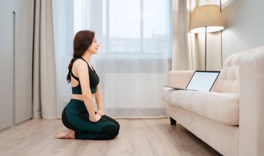 Sporcu evinde oturuyor ve dizüstü bilgisayarda fitness dersleri alıyor.