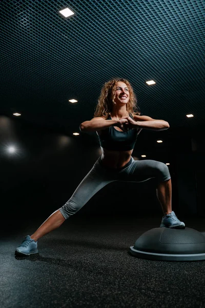 Kvinna i gymmet gör fitness gör knäböj på en balanseringsplattform. Stockbild