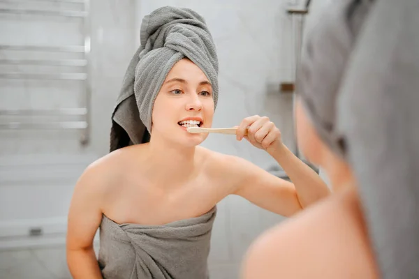 Jonge vrouw voert ochtendverzorging in de badkamer poetsen haar tanden. Stockafbeelding