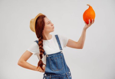 Çiftçi, beyaz arka planda sebzelerin kalitesini değerlendiren bir balkabağı tutuyor..