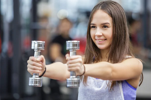 Mujer joven haciendo ejercicio con dos pesas en un gimnasio —  Fotos de Stock