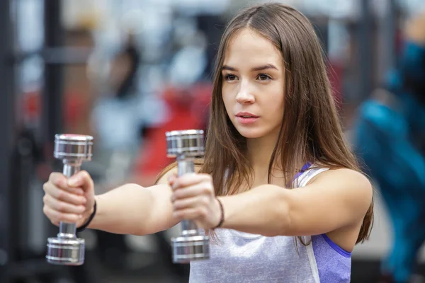 Mujer joven haciendo ejercicio con dos pesas en un gimnasio —  Fotos de Stock