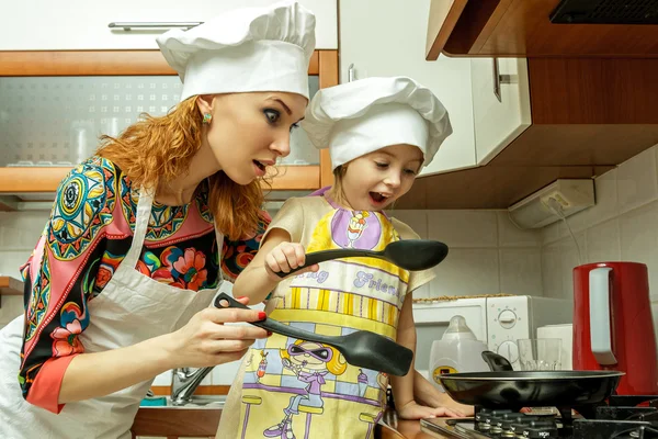 Moeder en dochter in witte chef-kok hoeden koken in de keuken. — Stockfoto