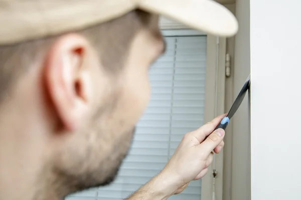 Macho sostiene cuchillo masilla en la pared cerca de la esquina de la pared . — Foto de Stock