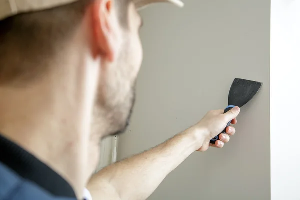 Macho sostiene cuchillo masilla en la pared cerca de la esquina de la pared . — Foto de Stock