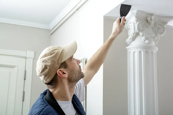 Worker holds putty knife and measures the wall corner using metal angle. — Stock Photo, Image