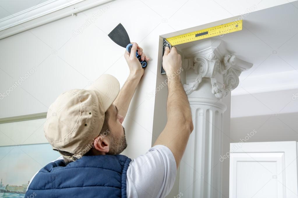 Worker holds putty knife and measures the wall corner using metal