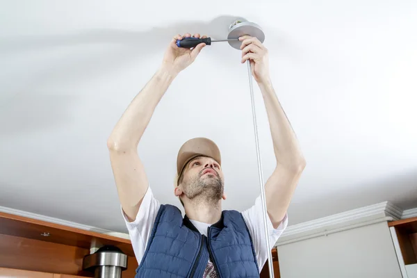 Un electricista macho que fija la luz en el techo con destornillador . — Foto de Stock