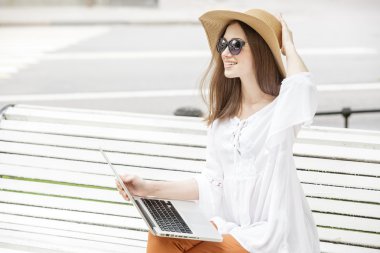 Bir bankta oturan bir dizüstü bilgisayar ile çalışan mutlu genç kadın. 