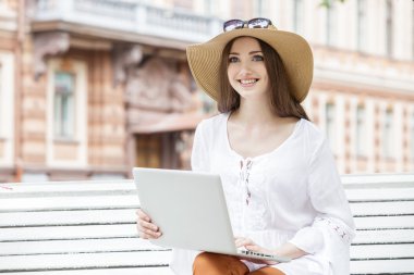 Bir bankta oturan bir dizüstü bilgisayar ile çalışan mutlu genç kadın. 