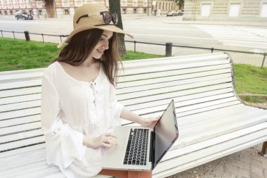 Bir bankta oturan bir dizüstü bilgisayar ile çalışan mutlu genç kadın. 