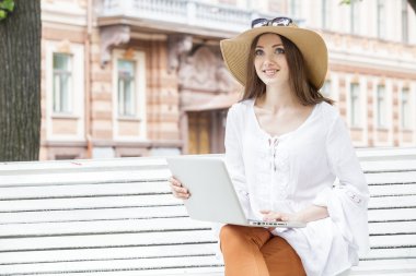 Bir bankta oturan bir dizüstü bilgisayar ile çalışan mutlu genç kadın. 