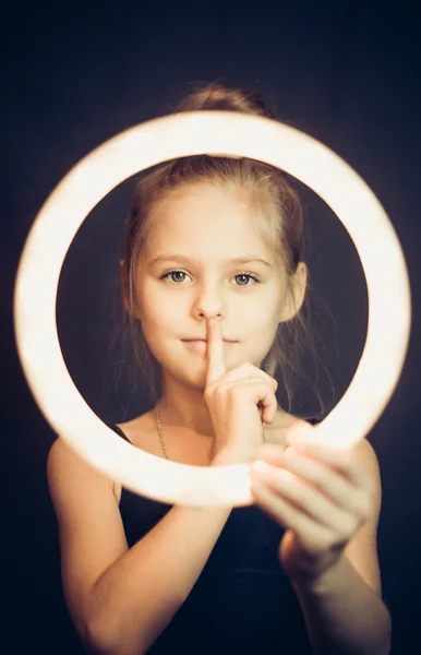 Beautiful young girl gymnast holding a glowing circle and making quiet gesture — Stock Photo, Image