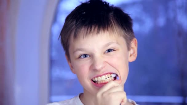 Хлопчик на синьому фоні чистить зуби, а потім розмовляє зубами — стокове відео