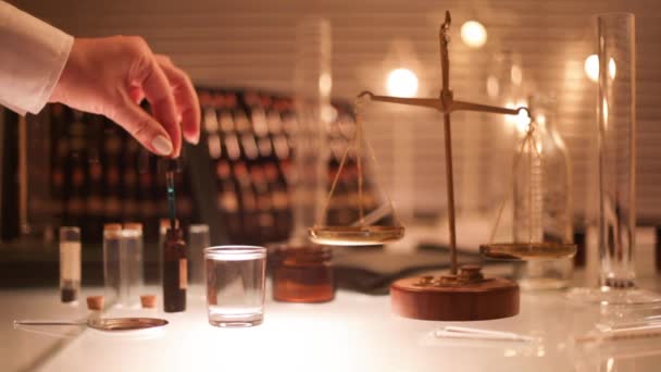 The old pharmacy or laboratory. Hand dripping into a glass blue liquid on the background of old pharmaceutical scale. — Stock Video